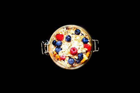 Muesli with blueberries and raspberries in glass jar on black background. The concept of  healthy...