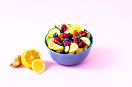 Fruit salad of wild berries and exotic fruits on pink background. The concept of a healthy diet,...