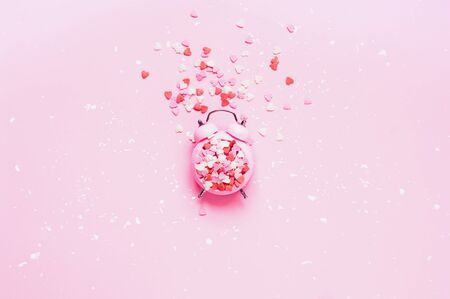 Valentines Day. Festive concept on pink background with heart shaped sweet confetti with alarm clock. Close-upの写真素材