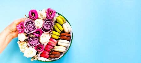 Festive composition. Female hand holds gift box with roses and macaroons. Valentines day concept. Close-up, copy spaceの写真素材