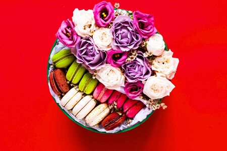 Festive concept from rosebuds in full bloom and Multicolored Macaroons on red background. Valentines Day. Template mock up of greeting card or text design. Close-up, copy spaceの写真素材