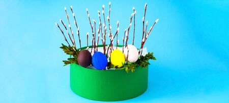Colorful easter eggs and willow branches in gift box on blue background. Festive concept,...