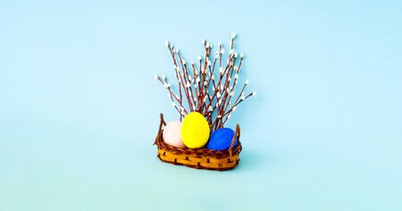 Abstract easter composition. Colorful eggs and willow branches in wicker basket on blue background....