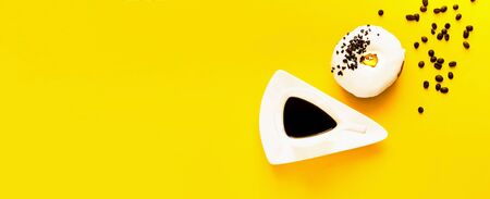 Black coffee in vintage white cup with chocolate donut on bright yellow background.Close-up