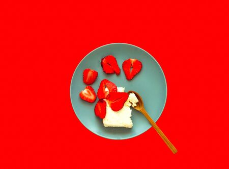 Cottage cheese dessert with strawberries in blue plate on red background. Healthy eating concept. Close-up, copy spaceの写真素材