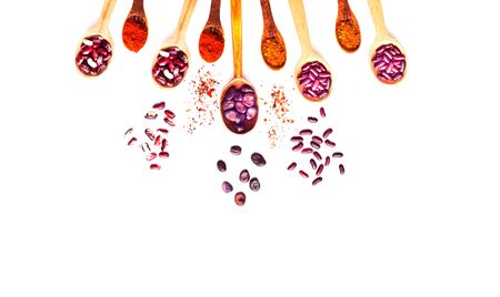 Wooden spoons with purple beans and spices on a white isolated background. The concept of useful products. Close-up, copy spaceの写真素材