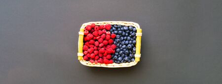 Blueberries and raspberries in wicker basket on dark background. The concept of ecological products.の写真素材