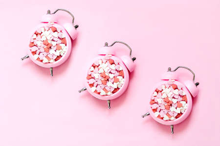 Pattern from a pink alarm clock with decorative colored hearts on pink background. Creative...