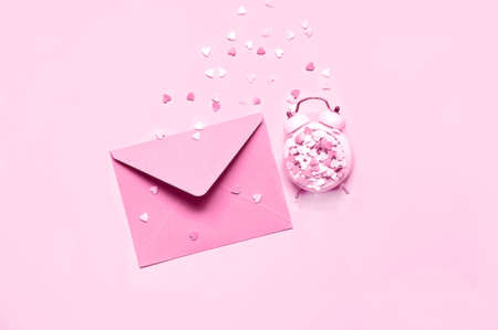 Pink alarm clock with decorative colored hearts and envelope on pink background. Festive concept or Romantic Love message. Monochrome. Creative copy spaceの写真素材