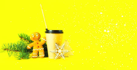 Coffee in paper cup with wooden tube and gingerbread man on trendy yellow background. Festive greeting card or Christmas decor. Creative copy space. Close-upの写真素材