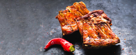 Spicy grilled spare ribs served with hot chili pepper on dark background. Top view. Creative copy...