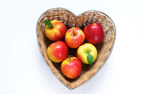 Red apples in straw basket made in the shape of heart on white background. Religious holidays concept - Jewish New Year or Apple spas. Copy spaceの写真素材