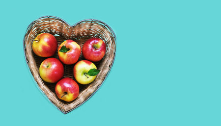 Red apples of wheat in bamboo basket made in the shape of heart on blue background. Religious holidays concept - Jewish New Year or Rosh Hashanah. Copy spaceの写真素材