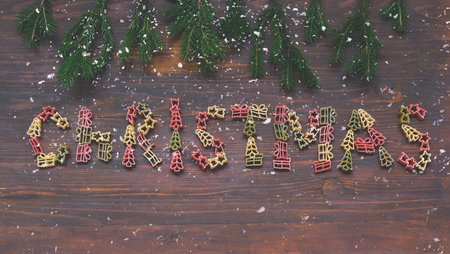 Christmas word fromTricolor pasta on wooden background with fir branches and snow. Creative space...
