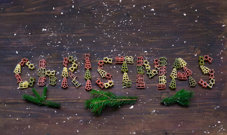 Christmas word fromTricolor pasta on wooden background with fir branches and snow. Creative space for design, blurred effectの写真素材