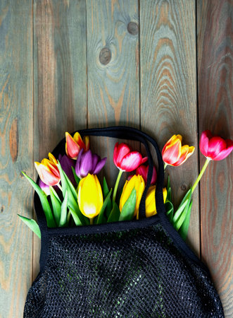 Colorful tulips in black shopping wicker bag on wooden table. Spring mood. Close-upの写真素材