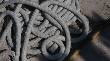 Tangled white climbing rope lying on concrete surface in sunlight and shadow.