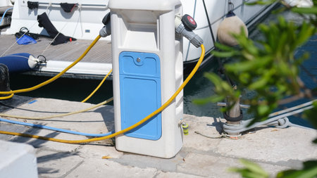 Power and water supply station on marina dock with yellow cables connected to a moored yachtの写真素材