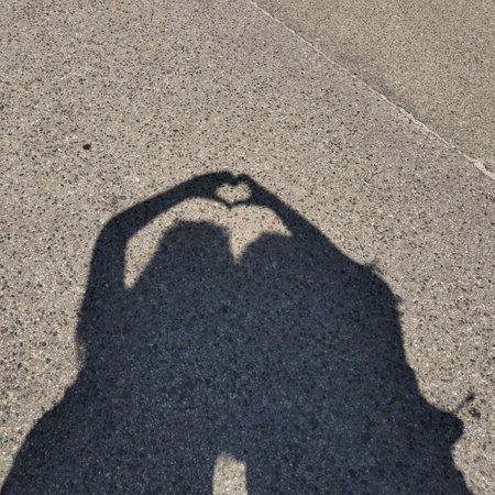 The shadow of friends on the asphalt. They created a heart-shaped hand gesture