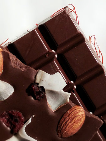 Two pieces of milk chocolate with almonds, coconut flakes, dried cranberries and chili flakes on a white backgroundの写真素材