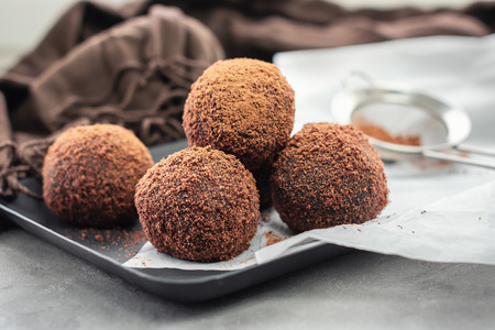 Cocoa balls, chocolate balls cakes in a black tray, sprinkled with cocoa powder.
