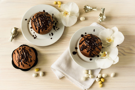 Chocolate muffins and white orchids on a light wooden background