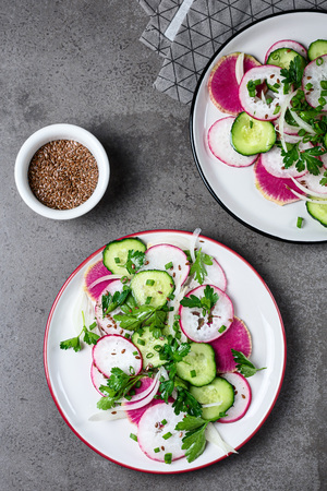 Summer salad with radishes, cucumbers and onions on a dark background.の写真素材