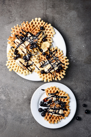 Waffles with chocolate, banana and berries on a white plate on a gray table.の写真素材