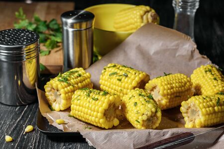 Boiled sweet corn with spices and herbs on a dark wooden table.