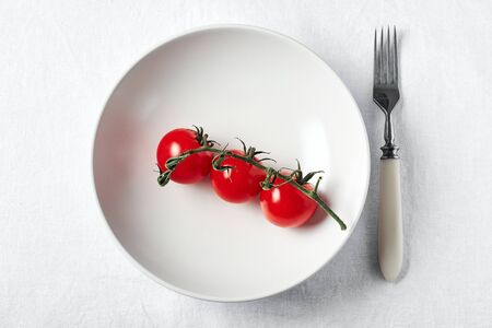 Fresh red cherry tomatoes on a white plate. Raw food diet concept.の写真素材