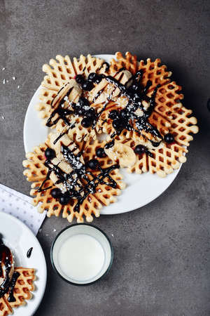 Homemade waffles with chocolate, banana and berries on a white plate.