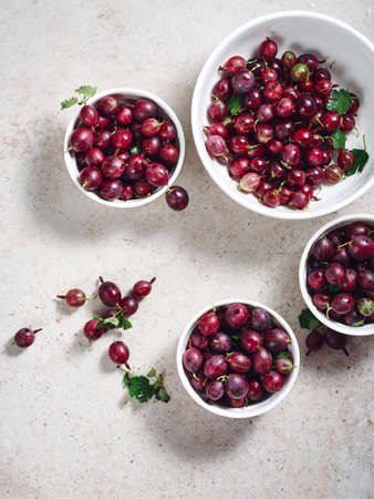 Ripe fruits of red gooseberries in white bowls on a light stone background.の写真素材