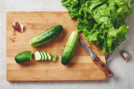 Fresh cucumbers and lettuce on a cutting board, top view.の写真素材