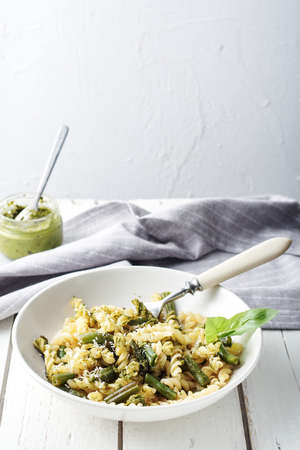 Fusilli pasta with green beans, pesto and basil on a white wooden table.の写真素材