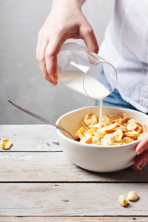 Female hands pour milk into a bowl of breakfast cereal.