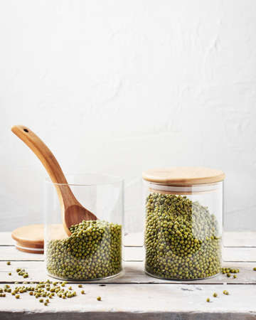 Two glass jars with raw mung beans on a wooden table.の写真素材