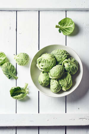 Fresh raw brussels sprouts in a bowl on a white wooden table, top view.の写真素材