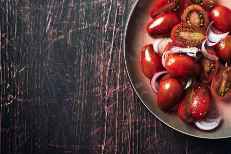 Salad with cherry tomatoes and onions on a dark wooden background, top view.の写真素材