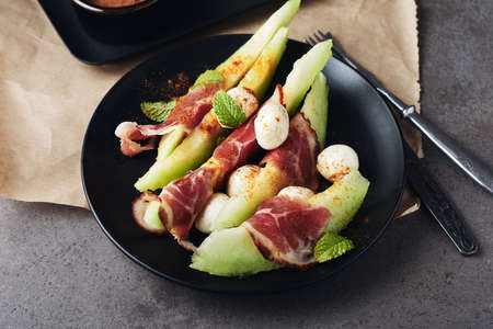 Melon with prosciutto, mozzarella balls and mint on a dark background.の写真素材