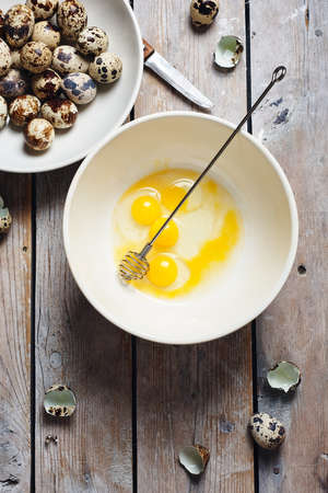 Broken quail eggs in a bowl on a wooden background.の写真素材