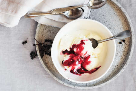 Vanilla ice cream with elderberry sauce in a bowl on a linen tablecloth, top view.