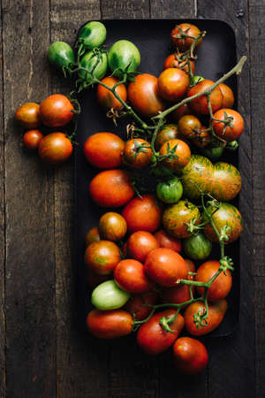 Fresh red and green tomatoes in a tray on a wooden background.の写真素材
