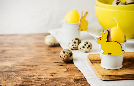Easter table decoration close-up. Yellow candle egg, bunny and quail eggs.