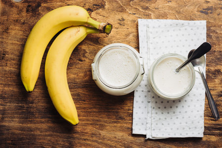 Two jars of banana yogurt on a wooden table.の写真素材