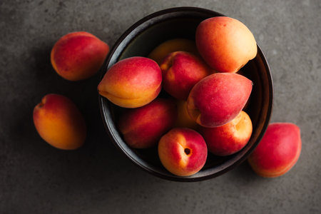 Fresh apricots in bowl on dark background, close-up.