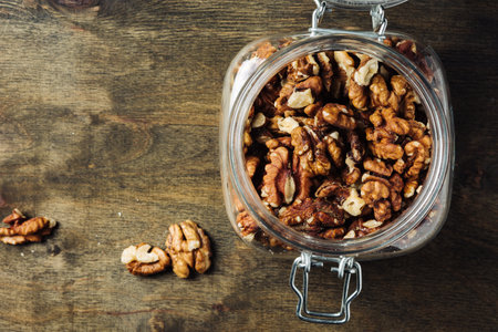 Shelled walnuts in jar on wooden background.