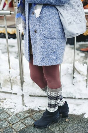 Girl in grey coat, hat and blanket scarf with cup of coffee near carousel, winter street style lifestyleの写真素材