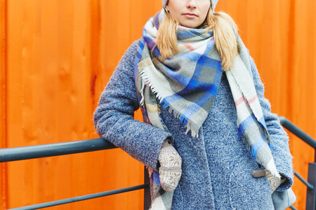 Girl in grey coat, hat and blanket scarf on orange background winter street style lifestyle