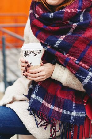 Girl in blanket scarf with coffee sitting in puplic spaceの写真素材