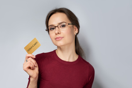 Young woman in red jumper in glasses holding gold gard isolated on gray backgroundの写真素材